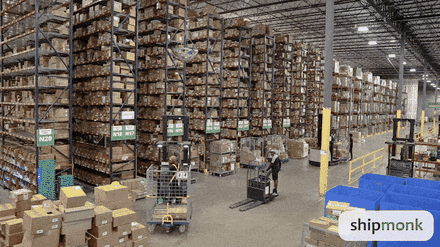 A busy commodity warehouse with tall racks of stock and workers moving pallets.