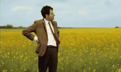 Mr. Bean standing in an empty field, checking his watch and waiting.